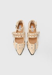Bežne balerinke z ostrim nosom, z več srebrnimi zaponkami in očesci, označene z imenom Steve Madden, prikazane na beli podlagi.