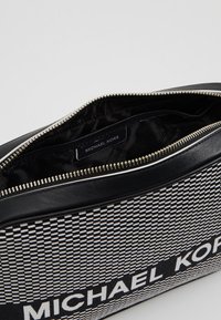 Black and white patterned clutch bag with leather trim, zip closure, and interior label. Features a textured woven design and soft lining.