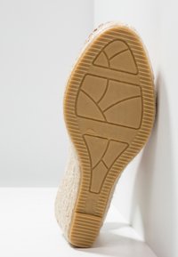 Semelle d'une chaussure compensée beige tissée avec un dessous en caoutchouc texturé indiquant la taille 37 et la mention "Fabriqué en Espagne".