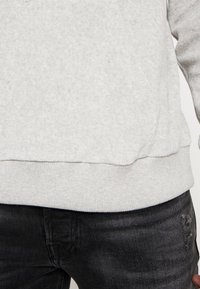 Sudadera gris claro con puños y dobladillo de canalé; hecha de un tejido suave. Combinada con jeans gris oscuro que presentan detalles desgastados.