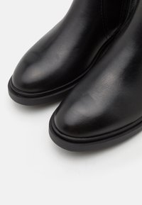 Stivaletti neri in pelle con punta arrotondata, texture liscia e suola in gomma bassa; presentano cuciture sottili lungo i lati.