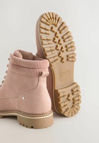 Las botas de tobillo de ante rosa presentan un cuello de punto texturizado, una robusta suela de goma con diseño de tracción y detalles de hardware en plata.