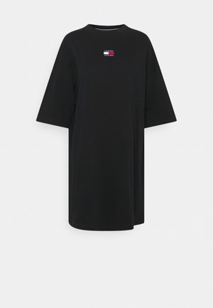 Czarna, oversize sukienka w formie T-shirtu z półdługimi rękawami i małym logo Tommy Jeans w kolorach czerwonym, białym i niebieskim na środku klatki piersiowej.