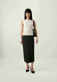 T relevant white ribbed sleeveless top, asorta cu o fustă neagră până la genunchi. Modelul poartă o geantă de mână neagră și pantofi cu toc înalt negri.