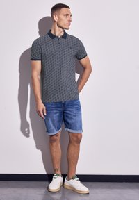 Polo de color azul marino con cuello navy, decorado en tonos de azul y crema. Combinado con pantalones cortos de mezclilla enrollados y zapatillas blancas con detalles en verde.