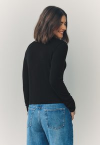 Black long-sleeve top with a ribbed texture, paired with high-waisted light blue jeans featuring back pockets and a slight fade.