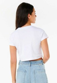 Camiseta blanca de corte cropped con mangas cortas, con un escote redondo y una textura suave, combinada con pantalones cortos de mezclilla de tiro alto.