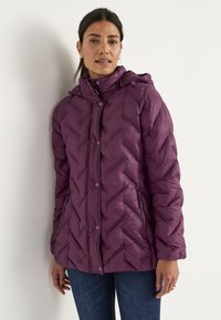 Lila puffjacka med chevronmönster, dragkedja och tryckknappar, justerbar huva, två sidofickor, bärs över en svart topp och jeans.
