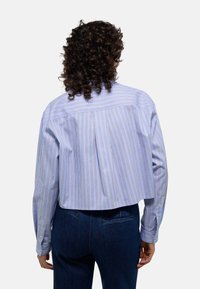 Chemise coupée à rayures bleues et blanches avec des manches longues, comportant un empiècement au dos et des poignets boutonnés, fabriquée en tissu léger.