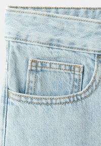 Poche de jean en denim bleu clair avec couture visible et une petite poche cousue à l’intérieur de la plus grande poche au dos.