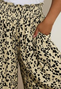 Leopardi kuosiset leveät housut, joissa on elastinen vyötärö, vaaleanbeige tausta ja tuntuvat mustat läiskät, sekä sivutaskut.