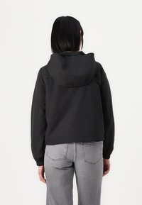 Czarna kurtka z kapturem o krótkim kroju i elastycznych mankietach. Materiał wydaje się gładki i lekki. Widok z tyłu ukazuje minimalne detale przes stitching.