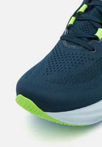 Scarpa da corsa navy con una tomaia in maglia traspirante, caratterizzata da dettagli perforati, accenti verde neon e una suola intermedia bianca testurizzata.
