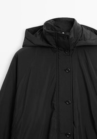 Cappotto nero con cappuccio, realizzato in tessuto leggero, con colletto alto, bottoni frontali e una texture liscia. Design semplice e funzionale.