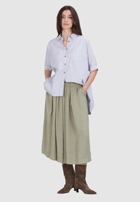 Lichtblauw button-up shirt met een voorzak, gecombineerd met een geplooide, knielange, olijfgroene rok en bruine haklaarzen.