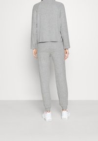 Szary zestaw dresowy składający się z długiego rękawa i dopasowanych spodni, wykonany z miękkiego materiału, z luźnym krojem i ściągaczami u dołu.