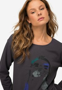 Camiseta de manga larga gris oscuro con un estampado gráfico de una cara de animal estilizada con acentos coloridos en azul y verde. Textura suave, cuello redondo.