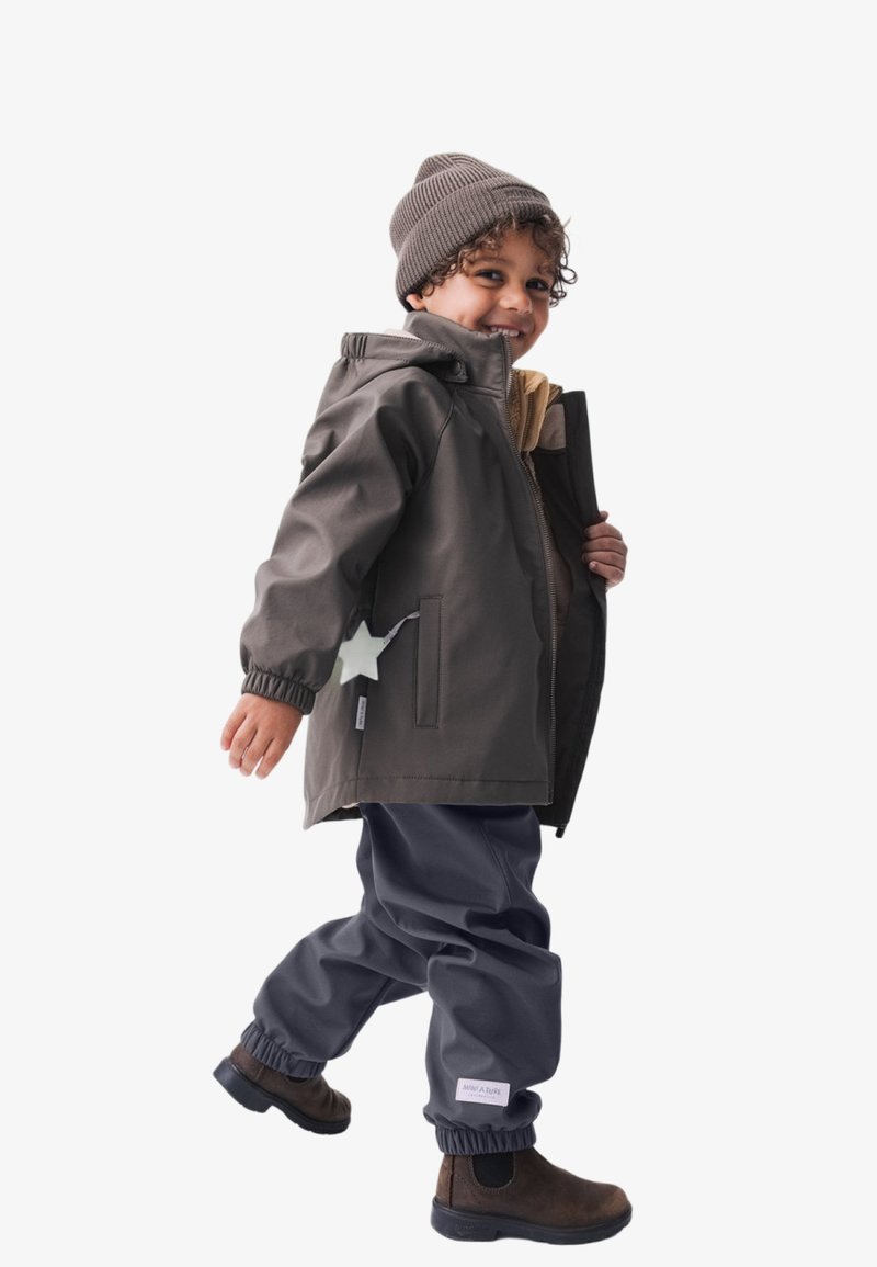 Graue wasserdichte Jacke mit einem Sternendetail, beigem Futter, kombiniert mit dunkelgrauen elastischen Hosen und braunen Stiefeletten. Braune Strickmütze.