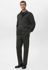 Cămașă cu nasturi din amestec de lână gri închis, cu guler și buzunar simplu pe piept, combinată cu pantaloni asortați și pantofi negri din piele.