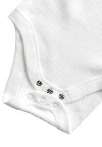 Monosie blanco con relieve y cuello redondeado, que presenta tres cierres metálicos a presión en la parte inferior para facilitar el vestido. Tejido de algodón suave.