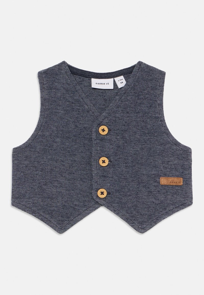 Gilet bleu marine en tissu texturé, avec un décolleté en V, trois boutons en bois et un petit patch en cuir sur le côté.