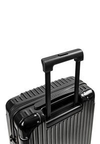 Czarna, twarda walizka z pionowymi żłobieniami, solidną, wysuwaną rękojeścią w dwóch krokach oraz zamknięciem na suwak. Posiada metalowe narożniki i zabezpieczający zamek.