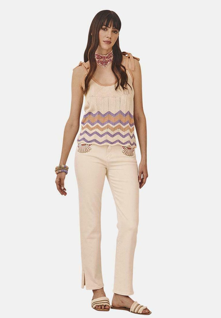 Top de punto ligero sin mangas con un patrón de zigzag púrpura, acompañado de pantalones crema con aberturas en los laterales y sandalias ligeras.