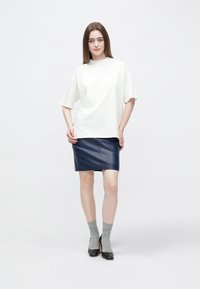 Bela prevelika bombažna majica, temno modra usnjena mini krilo, sive nogavice in črni salonarji, na nevtralnem ozadju.