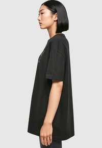 Black oversized t-shirt made of cotton. Short sleeves, round neckline, features minimalist graphic design on the front. Smooth texture.