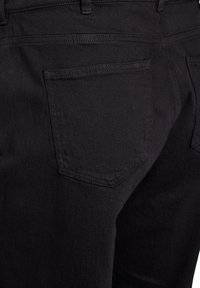 Black denim jeans feature a standard back pocket, slight texture, and contrasting stitching. The material appears sturdy with a smooth finish.