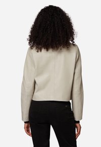 Ljusbeige läderjacka med croppad längd och en slät textur, sänkta axlar och enkla sömsdetaljer, kombinerad med svarta byxor.