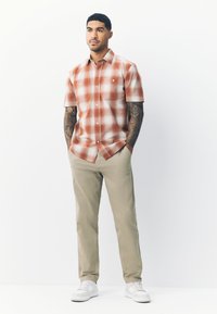 Camicia a maniche corte a quadri in arancione e bianco, con due tasche sul petto. Abbinata a pantaloni beige e scarpe da ginnastica bianche. Tessuto dalla trama liscia.