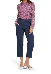 Paars geprinte blouse met lange mouwen en geplooide halslijn, gecombineerd met marineblauwe hoge taille broeken en witte puntige hakken.