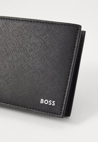 Black wallet made of textured fabric, featuring a subtle geometric pattern, white branding, and neat stitched edges.