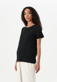 Black short-sleeve t-shirt with a round neckline, relaxed fit, and smooth texture, worn over a light-colored tiered skirt.