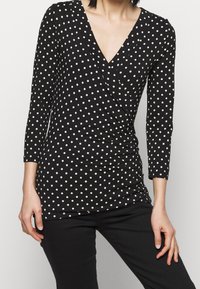 Mustapaita, jossa on pitkät hihat ja V-pääntie, valkoisia pilkkuja ja rypytystä vyötäröllä lisätekstuurin ja muodon vuoksi.
