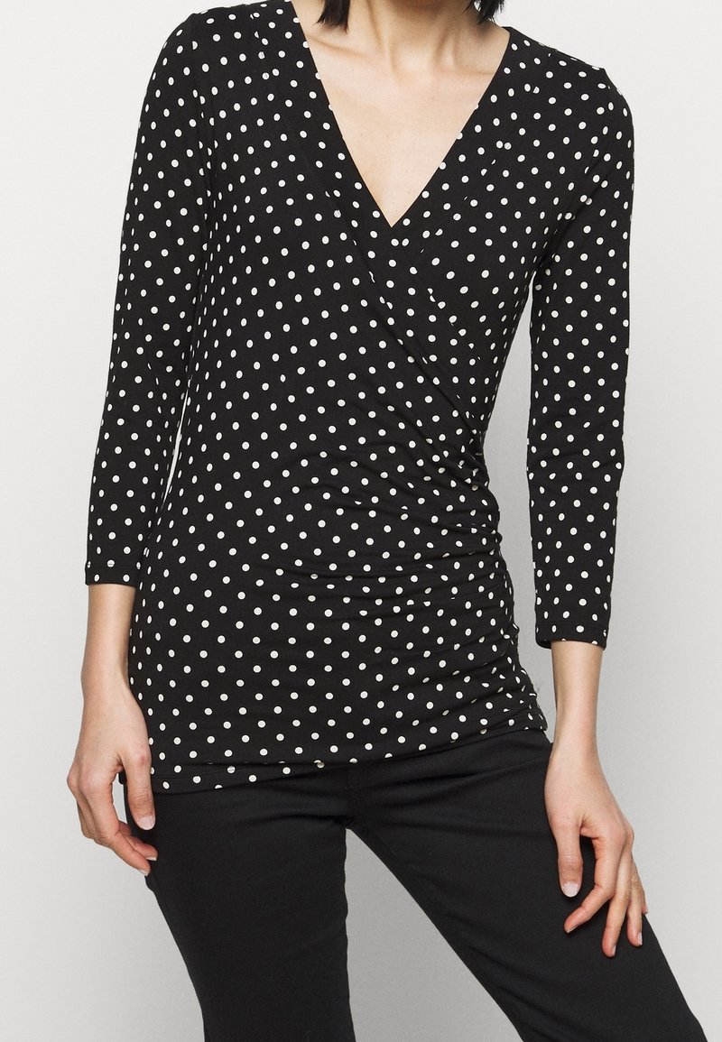 Mustapaita, jossa on pitkät hihat ja V-pääntie, valkoisia pilkkuja ja rypytystä vyötäröllä lisätekstuurin ja muodon vuoksi.