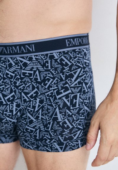 Sötétkék boxer alsó, amelyet betűk és logók ismétlődő geometriai mintázata díszít, sötét derékpánttal, amelyen az "Emporio Armani" felirat található.