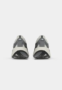 Et par grå og hvide Adidas sneakers set fra bagen, der viser sorte og hvide såler samt Adidas-logoet på hælflapperne.