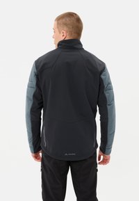 Giacca softshell nera con maniche imbottite blu chiaro, colletto alto e orlo leggermente curvato. Presenta un logo vicino al fondo.