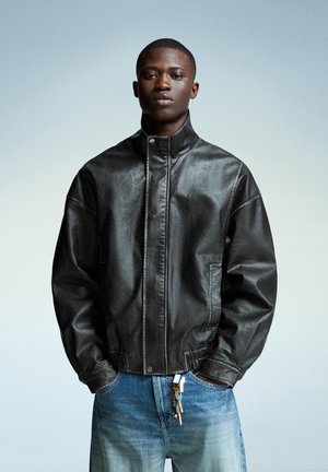 Black leather bomber jacket with front zipper, high collar, and elastic cuffs, paired with blue denim jeans. Keys hang from the waistband.