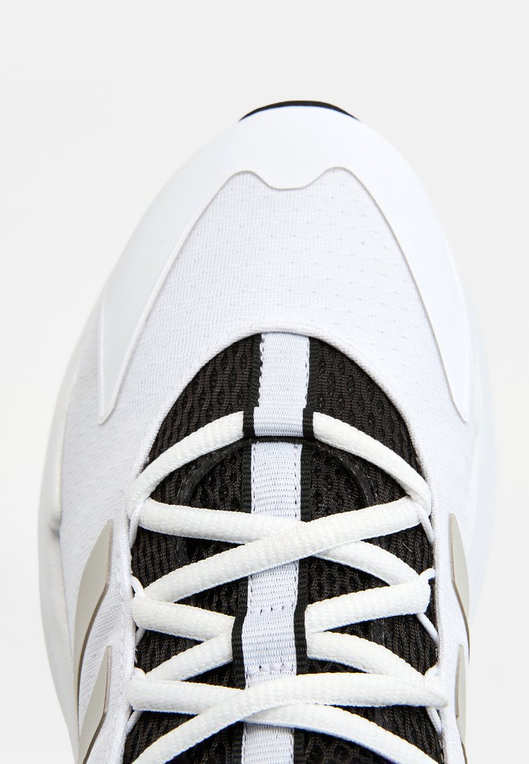 Chaussure de sport blanche et noire avec une tige en maille, une languette rembourrée et des rayures contrastantes sur un tissu texturé. Les lacets sont blancs.