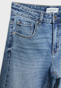 Jean en denim délavé avec un design à cinq poches, dotés de rivets en cuivre, d'un zip et de zones décolorées pour un contraste de texture.