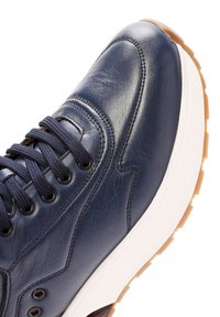 Marineblauwe leren sneaker met donkerblauwe veters, zwarte eyelets, witte tussenzool en lichtbruine loopzool.