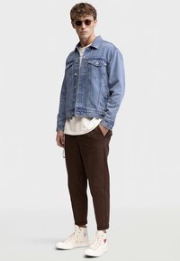 Svijetloplava traper jakna s dva džepa na prsima, bijela majica, smeđe sužene hlače i bijele tenisice visokog gazišta s naglascima.