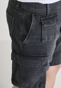 Shorts di denim neri con multiple tasche, taglio dritto e dettagli di cucitura visibili. Il tessuto ha una consistenza liscia e un aspetto sbiadito.