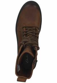 Bottine en cuir marron avec bout rond, devant à lacets, col rembourré et semelle en caoutchouc noir. L'intérieur présente le logo de la marque et un détail texturé.