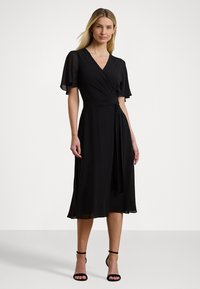 Black wrap dress with short, flutter sleeves. Made from soft fabric, features a tied waist and a flowy A-line skirt that ends mid-calf.