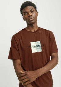 Brun T-shirt med afslappet pasform. Har et stort hvidt firkantet grafisk motiv med "JACK & JONES" tekst i sort. Korte ærmer, glat struktur.