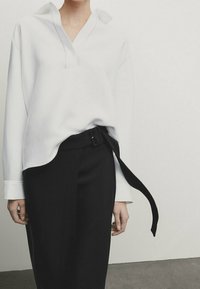 Camicia bianca a maniche lunghe con una vestibilità rilassata e colletto, abbinata a una gonna nera a vita alta con un dettaglio in vita annodato.